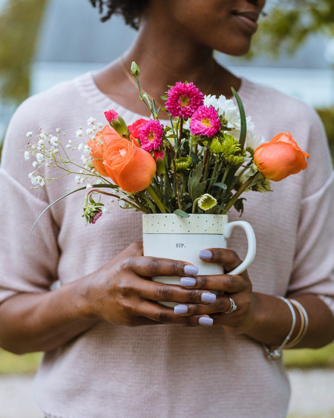 Person in a soft pink jumper holding a white mug of orange, pink and white flowers