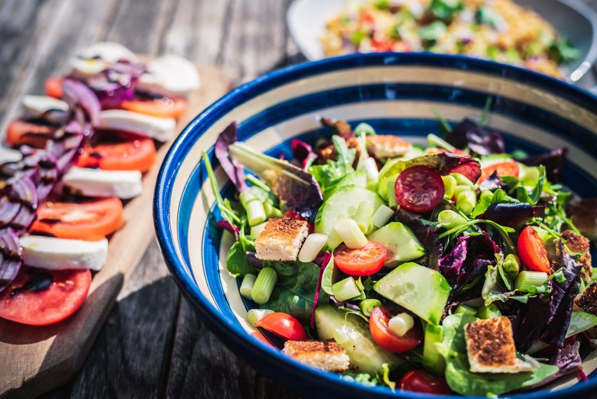Colourful mixed salad with tomatoes, cucumber and croutons in a blue bowl beside a tomato and mozzarella platter