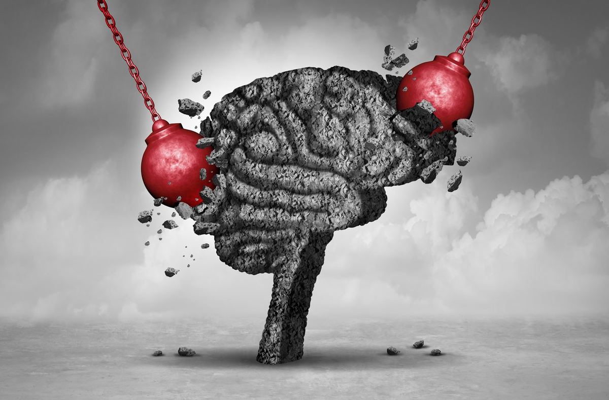 Two red wrecking balls smash into a crumbling concrete brain sculpture against a grey cloudy sky