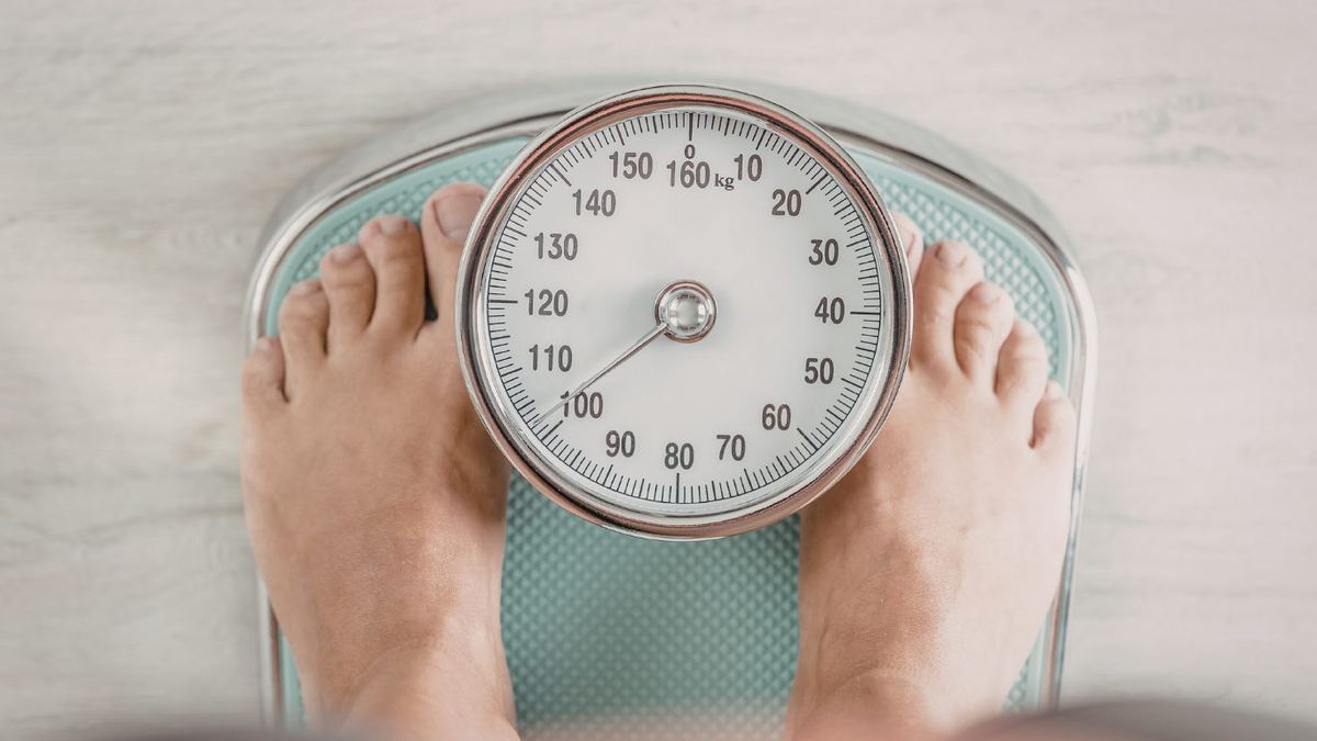 Bare feet standing on an analogue bathroom scale with the dial pointing to just over 100 kg