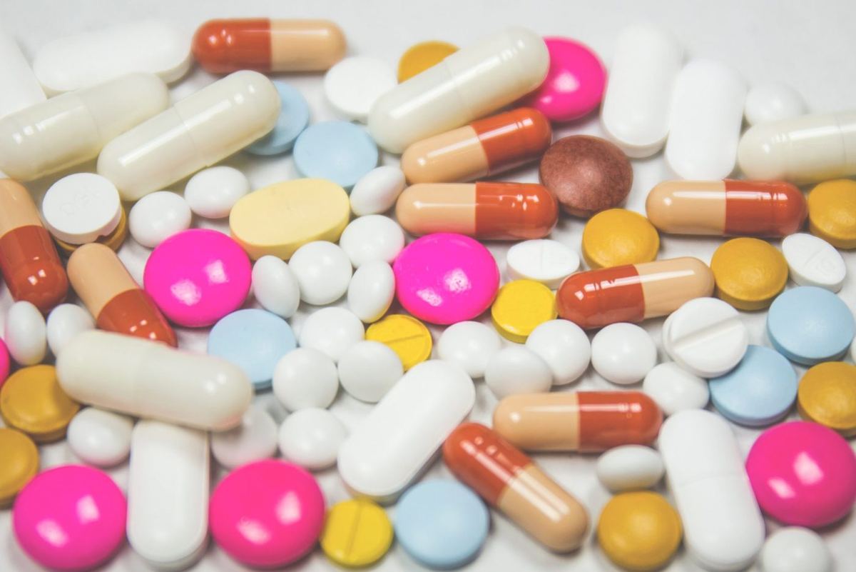 Colourful assortment of pills, tablets and capsules in various shapes and sizes scattered across a white surface