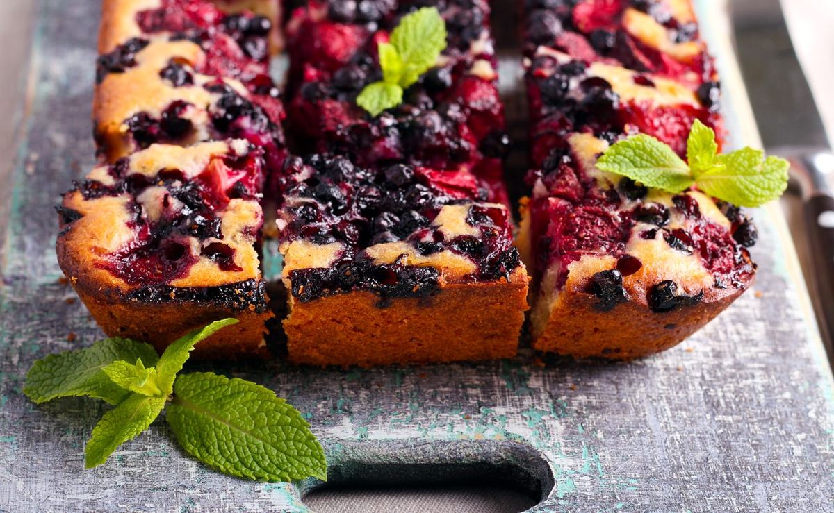 Sliced berry traybake with blueberries and raspberries, garnished with fresh mint, on a rustic wooden board