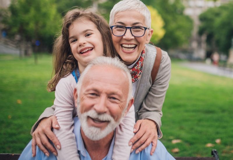 Smiling grandparents with their granddaughter in a park